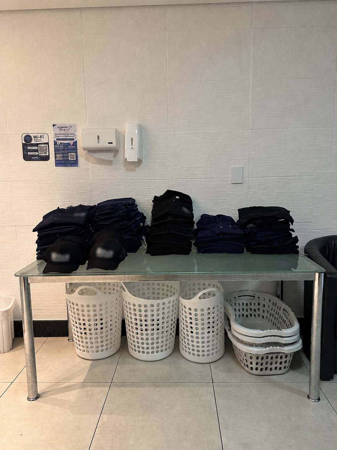 Volume de uniformes lavados e dobrados na lavanderia A Gente Lava, com cestos de roupa abaixo da bancada